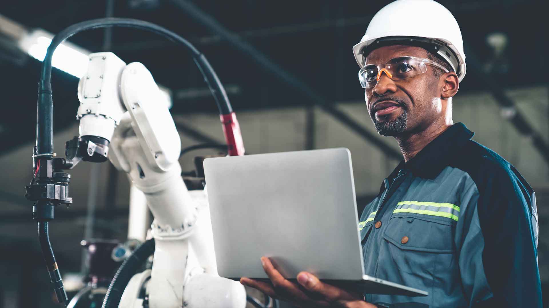 manufacturing technologist stands near robotic assembler and holds laptop