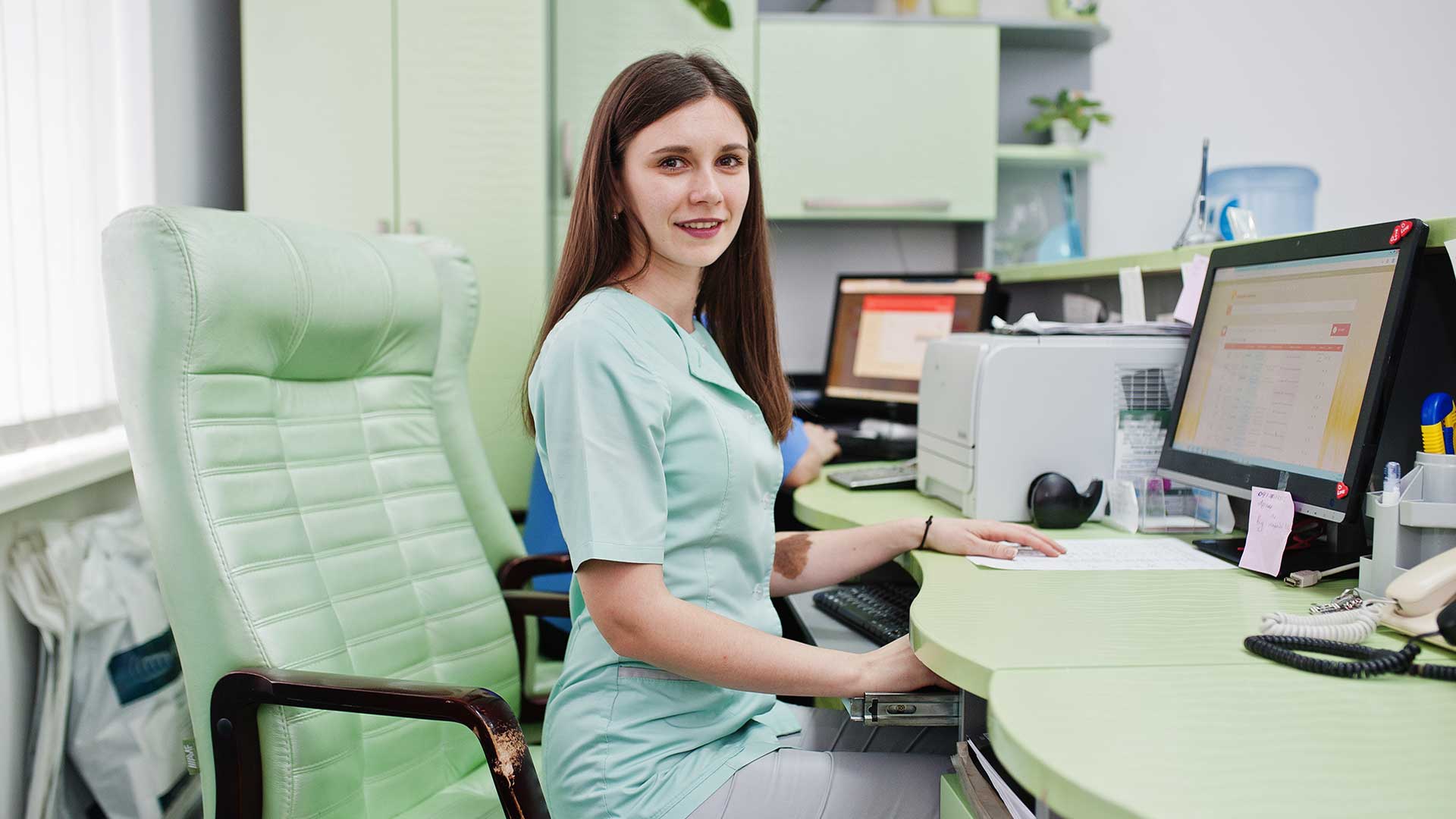 busy administrative worker in healthcare office sits at front desk monitor